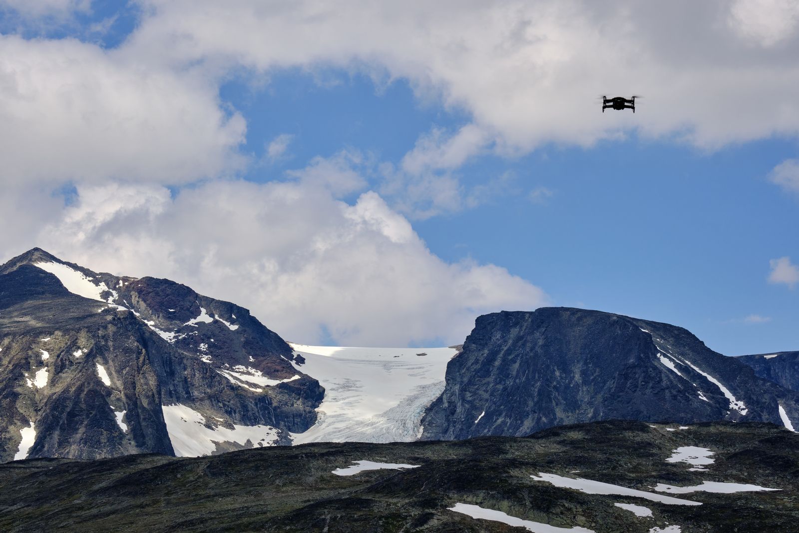 En drone svever over snødekte fjell i Jotunheimen