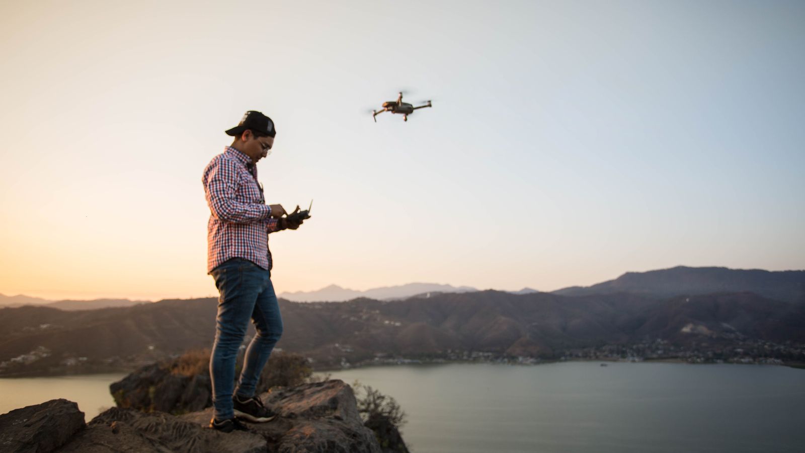 En dronepilot styrer dronen med fjernkontroll i solnedgang